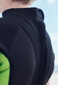 Fekete neoprénruha magas gallérral és zöld részlettel a bal oldalon, lapos varrással és cipzáras részlettel a hátoldalon.