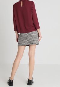 Burgundy blus med en nyckelhålsdesign bak, kombinerad med en mini kjol i svart och vit gingham. Skorna är svarta snörskor.