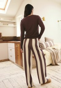 Maglia a maniche lunghe marrone e pantaloni larghi a righe in crema e marrone scuro, con vita elastica e vestibilità ampia.