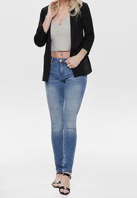 Musta bleiseri harmaan lyhyen topin päällä, yhdistettynä vaaleansinisiin slim fit -farkkuihin. Päällä mustat korkokengät. Silkkinen kangas, tiukka muotoilu.