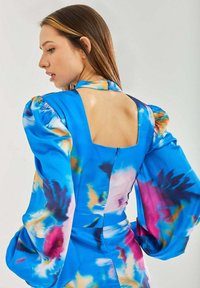 Colorful dress in blue with abstract patterns, puff sleeves, and a square back cut. Made from smooth fabric with a fitted waist.