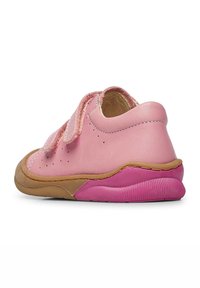 Chaussure en cuir rose avec une semelle en caoutchouc texturée, dotée d'une bride réglable en Velcro, de forme arrondie et d'accents roses contrastants sur le talon.