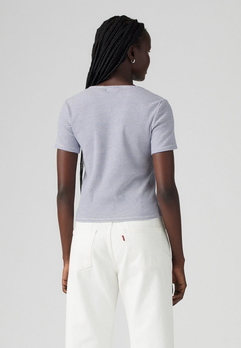 Haut à manches courtes à carreaux bleus et blancs avec un col rond, associé à un pantalon blanc taille haute. Tissu lisse, design ajusté.