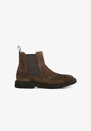 Bottine Chelsea en daim marron avec panneaux latéraux élastiques, patte de tirage et semelle plate en caoutchouc noir. Présente une texture lisse et un bout arrondi.