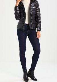 Sort puffjakke med en blank finish, lynlås lukning og hætte, parret med mørkeblå slim-fit jeans og sorte ankelstøvler.