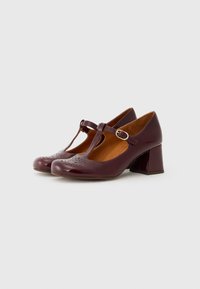 Burgundy patent leather heels with a T-strap, perforated detailing on the toe, and a block heel design.