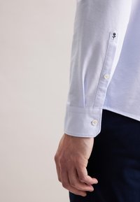 Witte lange mouwen shirt met een knoopmanchet, voorzien van een subtiele bloemenborduursel nabij de manchet, gemaakt van lichtgewicht stof.
