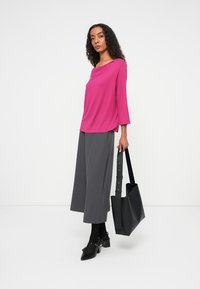 Top w kolorze fuksji z rękawami 3/4, szare szerokie spodnie, czarne obcasy i czarna torba tote. Całość o gładkiej fakturze.