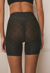 Black lace shorts featuring a textured floral pattern, mid-thigh length, and a smooth, fitted waistband.