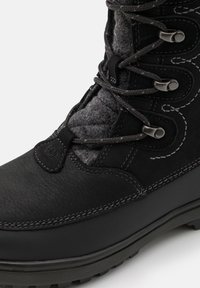 Bota impermeable negra con parte superior de cuero texturizado, forro de fieltro gris, herrajes metálicos y costuras en contraste, con suela de goma.