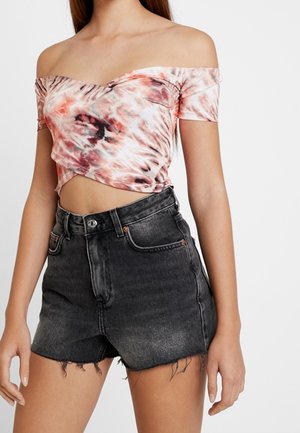 Off-the-shoulder, tie-dye kort topp i rosa och orange nyanser, parat med svarta högmidjade denimshorts med fransad nederkant.
