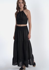 Zwart linnen twee-delig set bestaande uit een halternek crop top en een gelaagde maxi rok met een elastische tailleband, aangevuld met espadrilles.