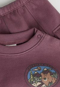 Lilla bomulds sweatshirts med ribbet halslinning og trykknaplukning, prydet med et rundt bjørnegrafik og bjergdesign på fronten.