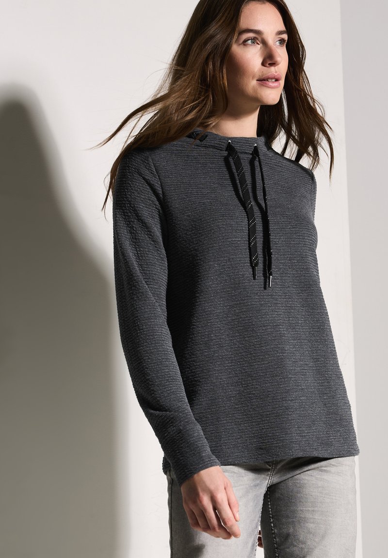 Mörkgrå texturerad hoodie med en lös passform, försedd med en dragsko i huvan och långa ärmar, kombinerad med ljusgrå jeans.