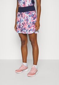 Flerfärgad blommig kjolshorts med midja i marinblått, kombinerad med ljusrosa löparskor med vita och blå detaljer.