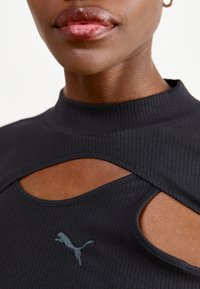 Svart ribbet høyhalset topp med utskjæringer og en liten blå Puma-logo på brystet.