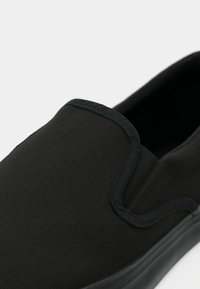 Mustad libisemiskindlad kingad, millel on tekstureeritud pealiskihid, minimaalsed õmblused ja nähtamatud paelad. Põhi on must ja sile, rõhutades selle lihtsat disaini.