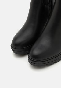 Botas de tobillo de cuero negro con un diseño elegante, que presentan una punta redondeada y una suela de goma gruesa, acentuadas por un cierre lateral.