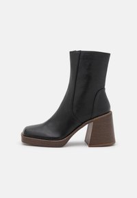 Bottines noires en cuir, dotées d'un bout arrondi et d'un talon en bois texturé, épais. Surface lisse avec un design élégant.
