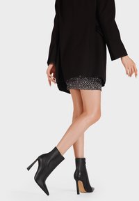 Stivali neri alla caviglia con una finitura in pelle liscia, punta affilata e alto tacco a stiletto. Il design presenta una zip laterale discreta.