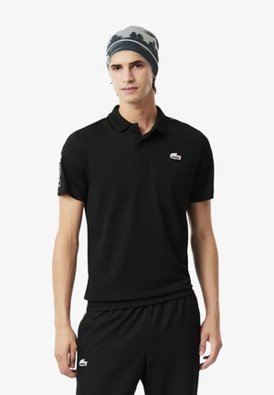 Zwarte polo met korte mouwen en een klassieke kraag, voorzien van een klein geborduurd logo op de borst. Gecombineerd met zwarte shorts.