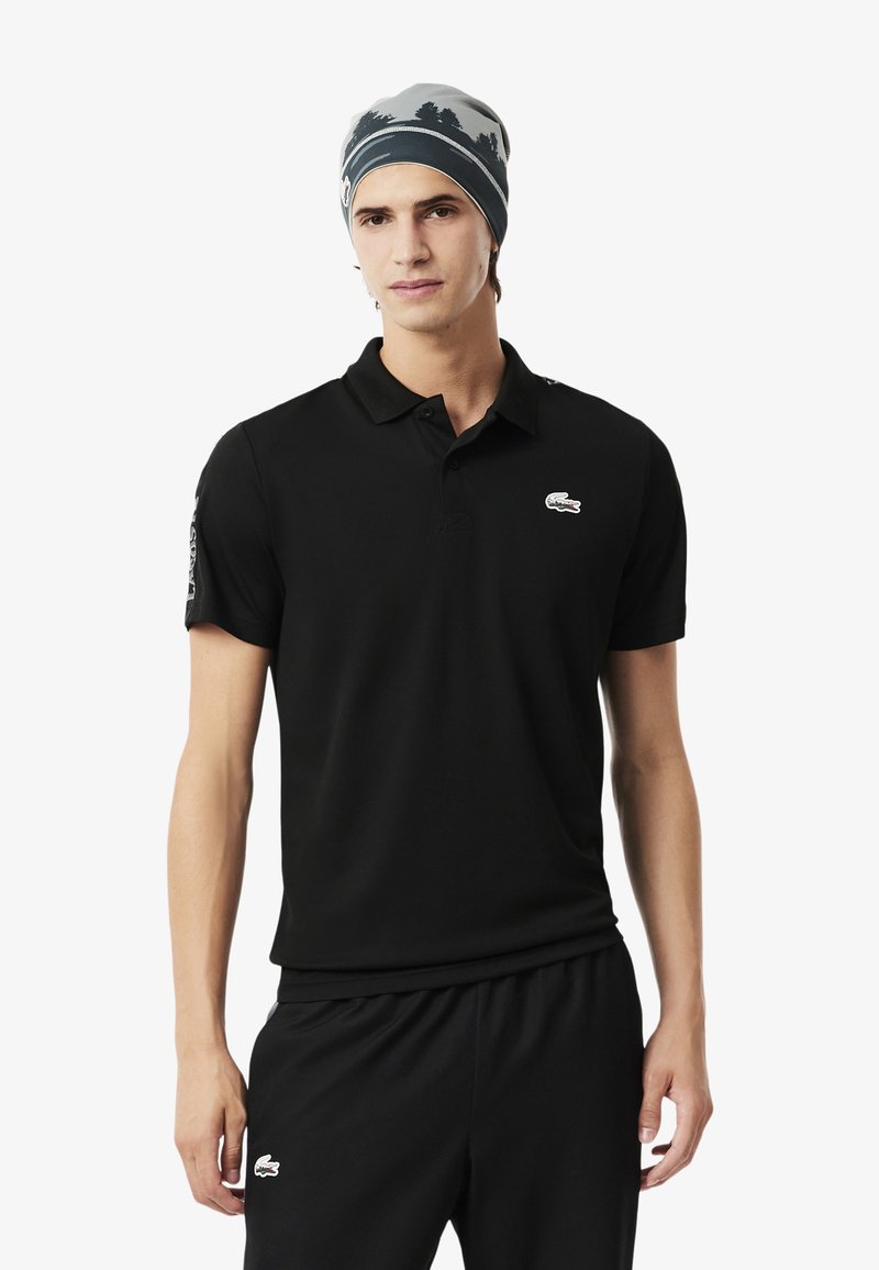 Polo shirt nera con maniche corte e colletto classico, decorata con un piccolo logo ricamato sul petto. Abbinata a pantaloni corti neri.