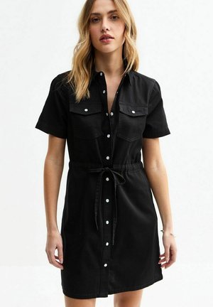 Black denim dress with short sleeves, button-up front, two chest pockets, and a cinched waist tied with a matching fabric belt.