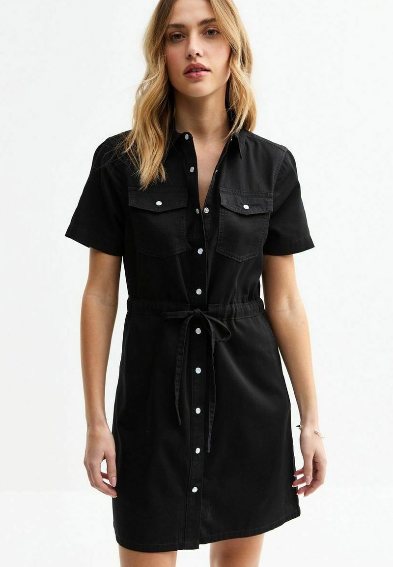 Black denim dress with short sleeves, button-up front, two chest pockets, and a cinched waist tied with a matching fabric belt.