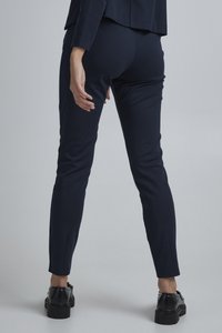 Knieblaue, taillierte Hosen mit glatter Textur, mit einer mittelhohen Taille und einem Schlitz am Knöchel, kombiniert mit schwarzen, klobigen Schuhen.