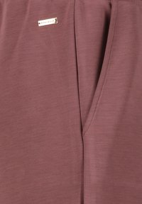 Bordeaux sportbroek met een gladde textuur, voorzien van een logo-etiket en een relaxte pasvorm. Inclusief een uniek ontwerp met subtiele plooien.