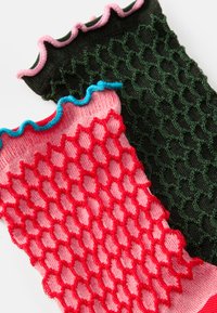 Polainas de malha em rosa e verde. O rosa possui um padrão de diamantes com borda de frufru azul; o verde tem um padrão texturizado com borda de frufru rosa.