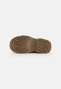 Sola de borracha castanha com um padrão texturizado em ziguezague; apresenta um detalhe circular de logótipo. Design plano adequado para vários terrenos.
