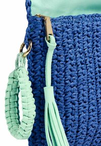 Borsa tessuta blu con una fodera verde menta, dotata di una cerniera dorata, una tracolla menta e un dettaglio a frangia. Materiale testurizzato e durevole.
