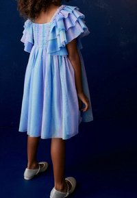 Vaaleanpunainen mekko röyhelöhihoilla, teksturoidulla kankaalla ja hienovaraisella kimalluksella. Mekossa on smokkattu selkä, ja se on yhdistetty harmaisiin ballerinoihin.