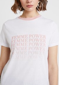 T-shirt en coton blanc avec un col côtelé rose, arborant le texte répété "FEMME POWER" avec une opacité varying sur le devant.