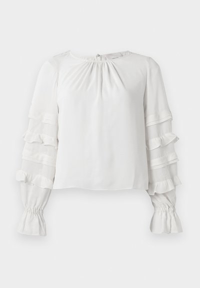 Camicia bianca a maniche lunghe con maniche a strati con volant, polsini arricciati e leggero arricciamento sul collo rotondo.