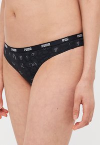Crne tangice s suptilnim uzorkom i elastičnim pojasom s "PUMA" logotipom u bijeloj boji. Mekana tekstura tkanine.