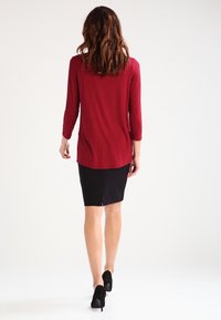 Rode langemouw top met een relaxte fit, gecombineerd met een zwarte pencil skirt. De outfit wordt compleet gemaakt met zwarte hoge hakken.