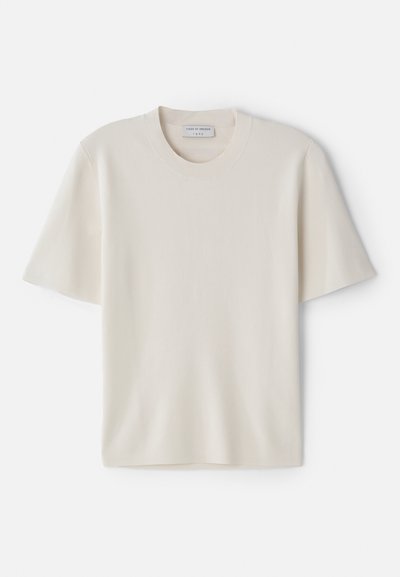 Krēmveidīga T-kreklu ar īsām piedurknēm, apaļo kakla izgriezumu, izgatavota no mīksta materiāla, ar taisnu griezumu un minimālu dekoru.