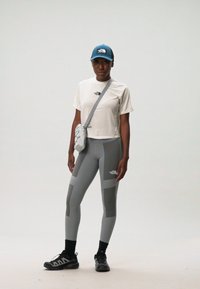 Treningsantrekk som består av en hvit kort t-skjorte, grå leggings med paneldetaljer, og en blå caps. Tilbehøret inkluderer en liten crossbody-veske.
