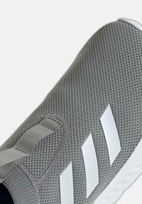 Chaussure de sport grise avec une tige en mesh respirant, dotée de trois bandes diagonales blanches, d'accents texturés et d'une semelle flexible.