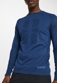 Marinblå långärmad träningsskjorta med ett strukturerat mönster på framsidan, lättviktsmaterial och kontrasterande sömmar. Logotyp på den nedre sidan.