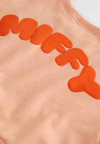 Virsikuvärviline dressipluus, millel on suured ümarad 3D oranžid tähed, mis moodustavad rinnal, kaeluse lähedal sõna "MIFEY".