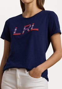 T-shirt de algodão azul marinho com mangas curtas e decote arredondado, apresentando um design bordado multicolorido "LRL" no peito.