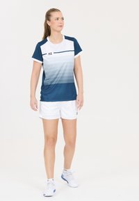 Urheilullinen lyhythihainen paita tummansinisenä, jossa on kevyt tumman sävyn gradientti, yhdistettynä valkoisiin shortseihin. Rinnassa ja shortseissa on FZ-logo.
