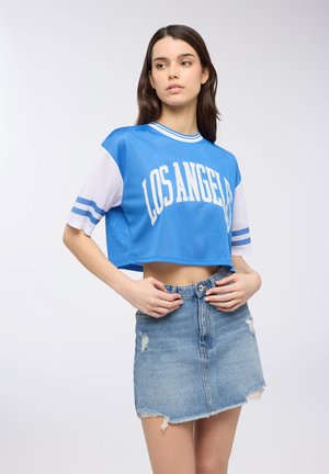 Maglia in jersey a rete blu cropped con stampa "LOS ANGELES", abbinata a una gonna di jeans distrutta. Presenta maniche bianche con strisce blu.