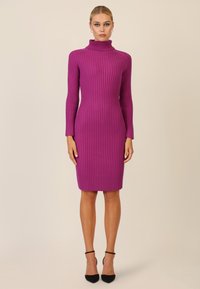 Abito a collo alto aderente in maglia a costine, colore viola vivace, maniche lunghe, lunghezza al ginocchio, texture liscia, abbinato a scarpe con tacco nere.