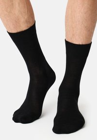 Schwarze Baumwollsocken, Knöchelhöhe, glatte Textur, gerippter Bund, enganliegendes Design, ohne Muster oder Akzente, mit einer Nahaufnahme auf den Beinen.