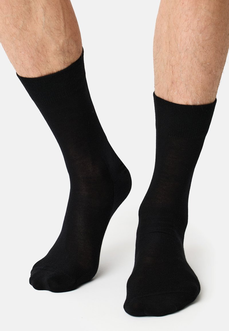 Schwarze Baumwollsocken, Knöchelhöhe, glatte Textur, gerippter Bund, enganliegendes Design, ohne Muster oder Akzente, mit einer Nahaufnahme auf den Beinen.