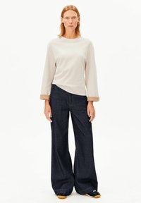 Hellgraues Langarmshirt mit rundem Halsausschnitt. Dunkelblaue Jeans mit weitem Bein. Turnschuhe mit schwarzen und gelben Akzenten. Glatte Stofftexturen.